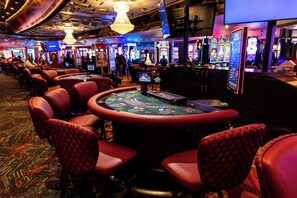 Une salle de casino avec des fauteuils rouges et moelleux, des machines à sous et une table de roulette.