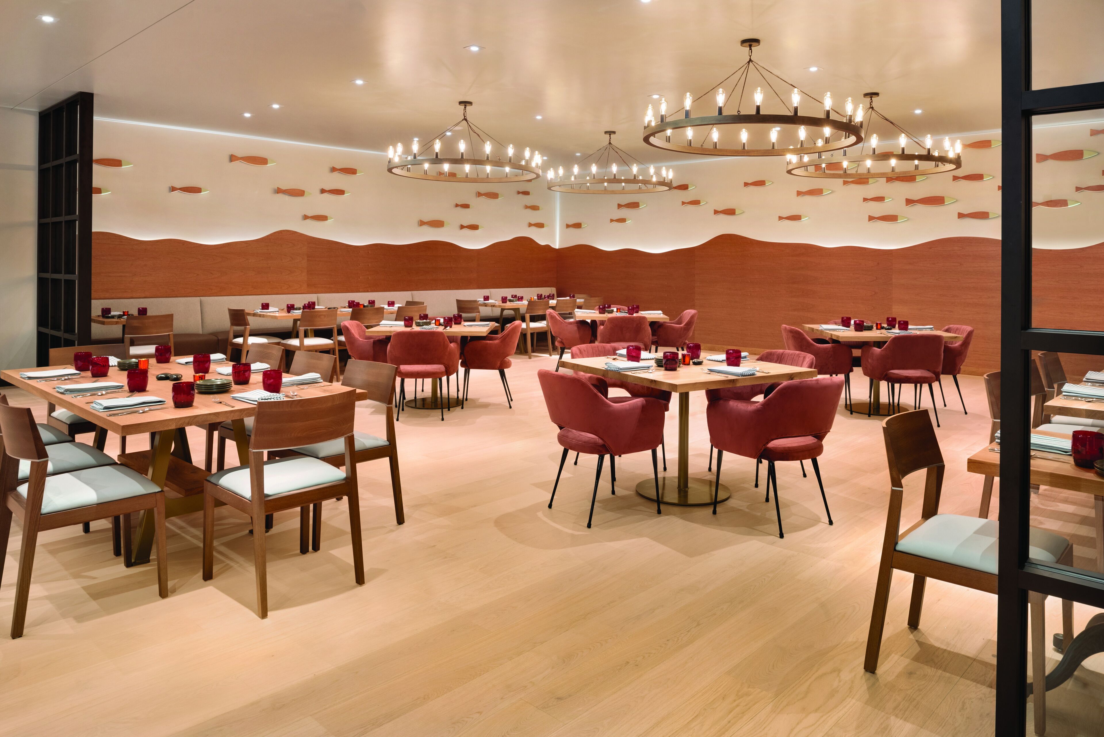 Un restaurant doté de nombreuses tables et chaises, d’un plancher en bois et de lustres modernes.