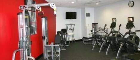 Ein Fitnessstudio mit Cardiogeräten, Krafttrainingsgeräten und einem Fernseher an der Wand.