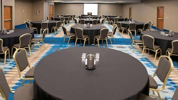 Un salón de conferencias con varias mesas redondas, cada una con sillas, una pantalla de proyector y un atril.