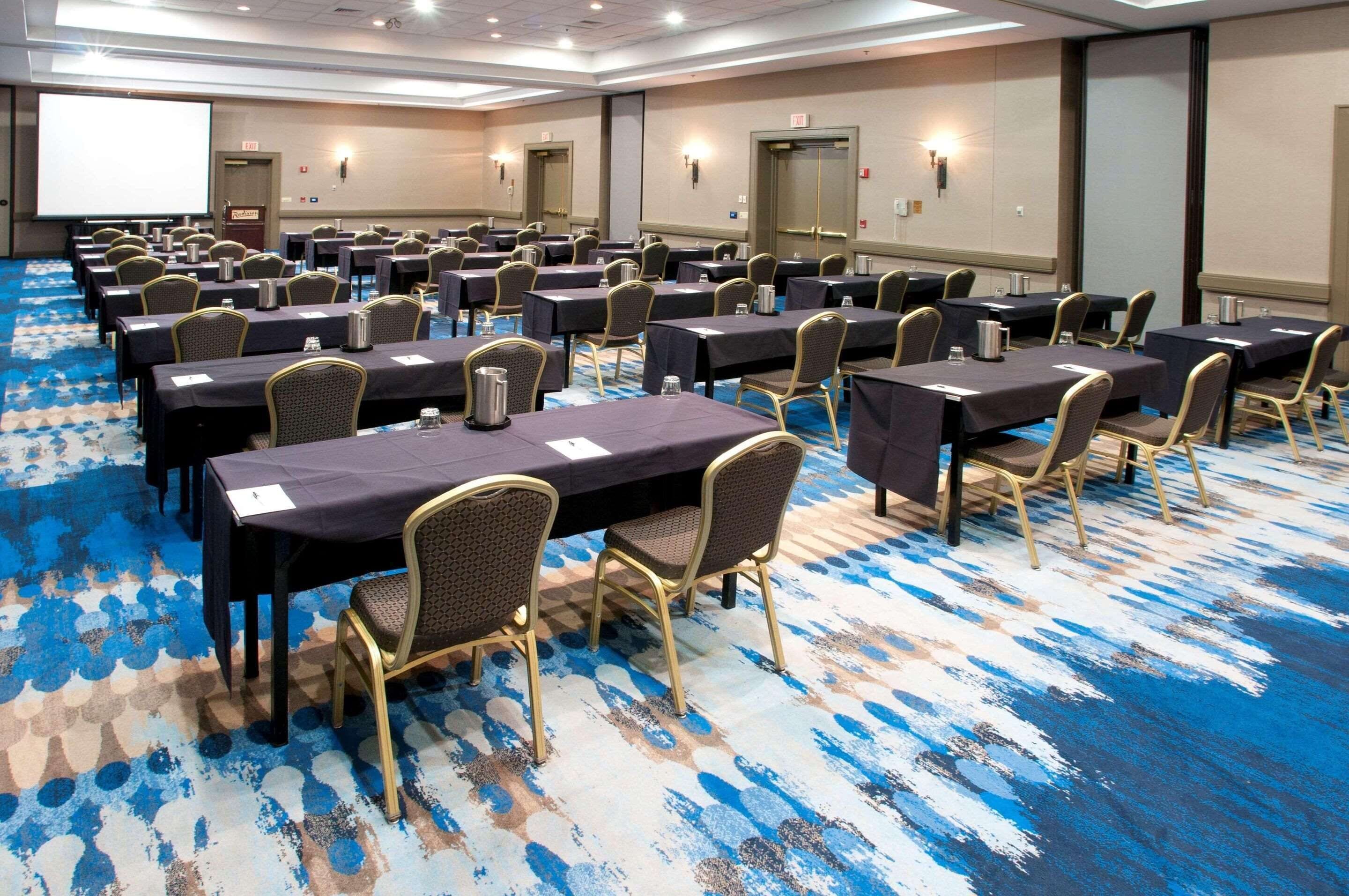 Une salle de conférence avec des rangées de tables et de chaises, équipée de bouteilles d’eau et de plaques nominatives.