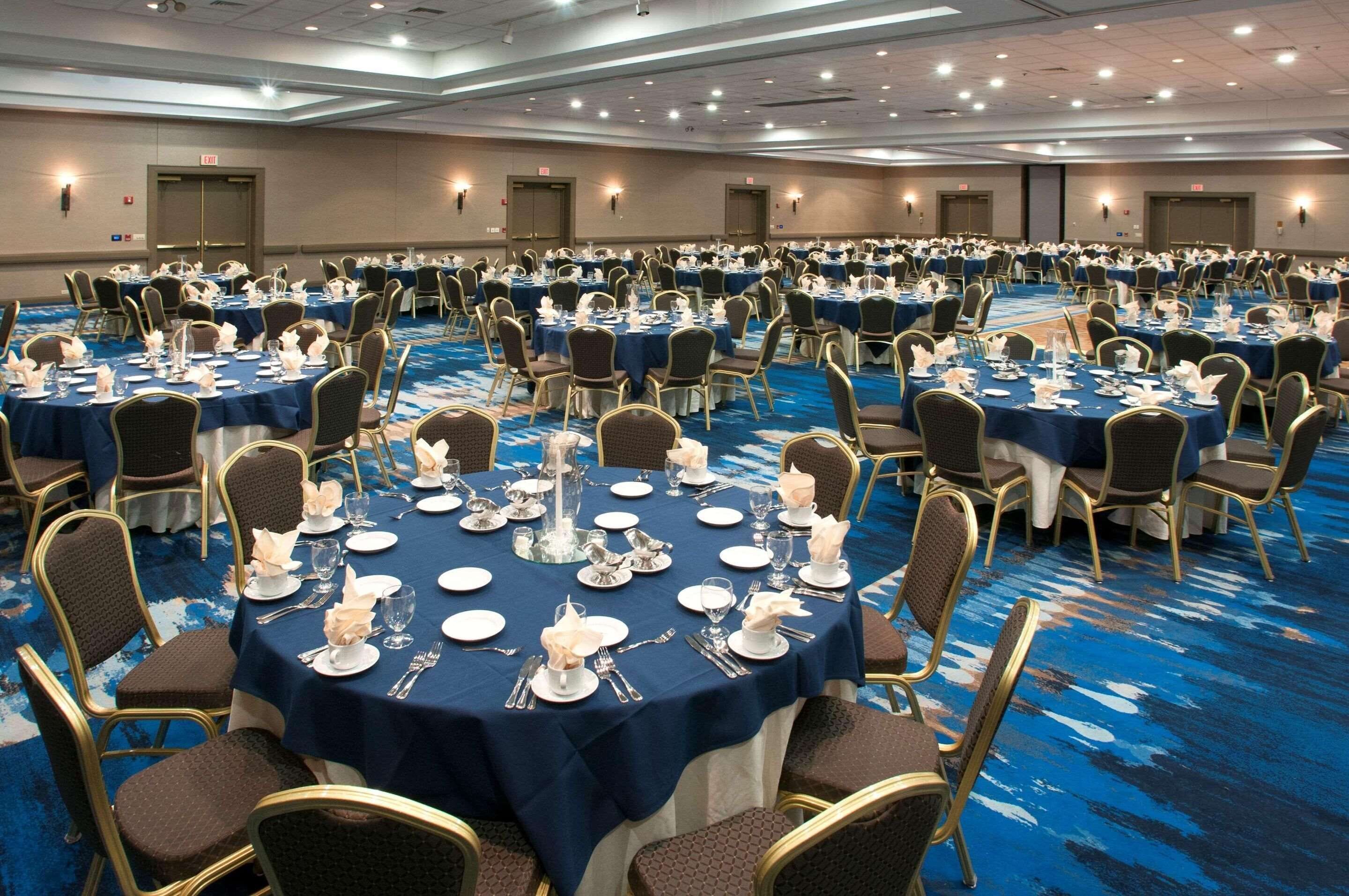 A large conference room with round tables set for dining, equipped with chairs and table settings.