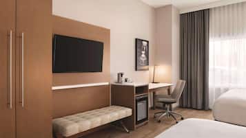 Une chambre d’hôtel comprenant un lit, un bureau avec une chaise, une télévision, un petit réfrigérateur et un banc.