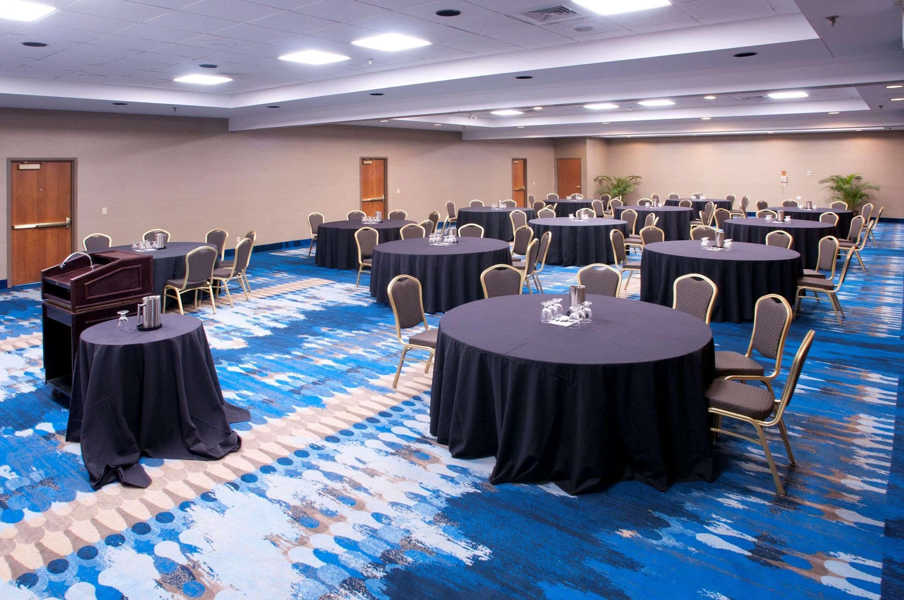 Une salle de conférence dotée de plusieurs tables rondes, chacune étant accompagnée de chaises et de nappes.
