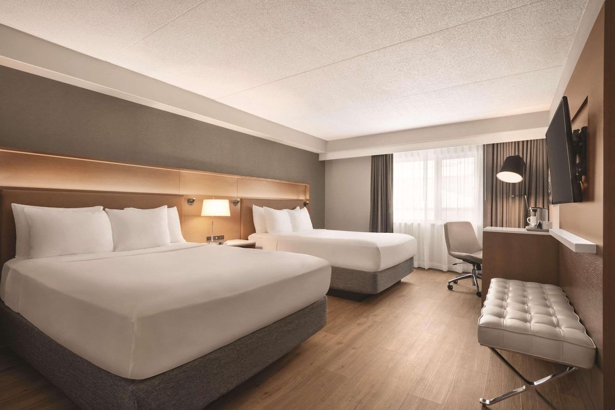 A hotel room with two beds, a desk, a chair, and a large window with curtains.