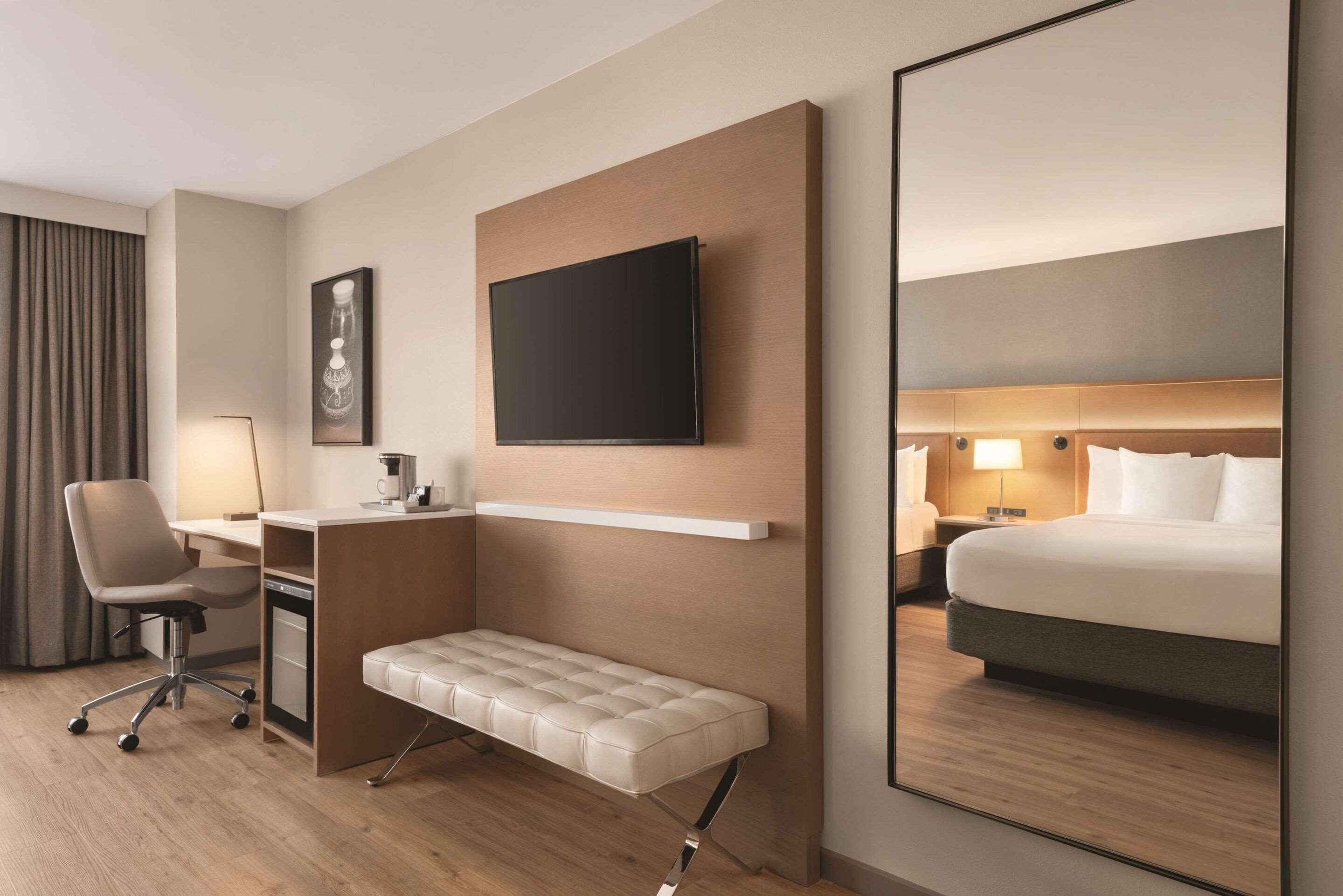 Een moderne hotelkamer met een groot bed, een bureau met stoel, een bankje, een flatscreen televisie en een spiegel.