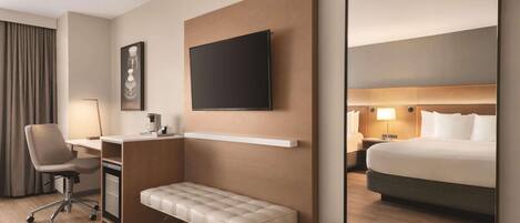 Een moderne hotelkamer met een groot bed, een bureau met stoel, een bankje, een flatscreen televisie en een spiegel.