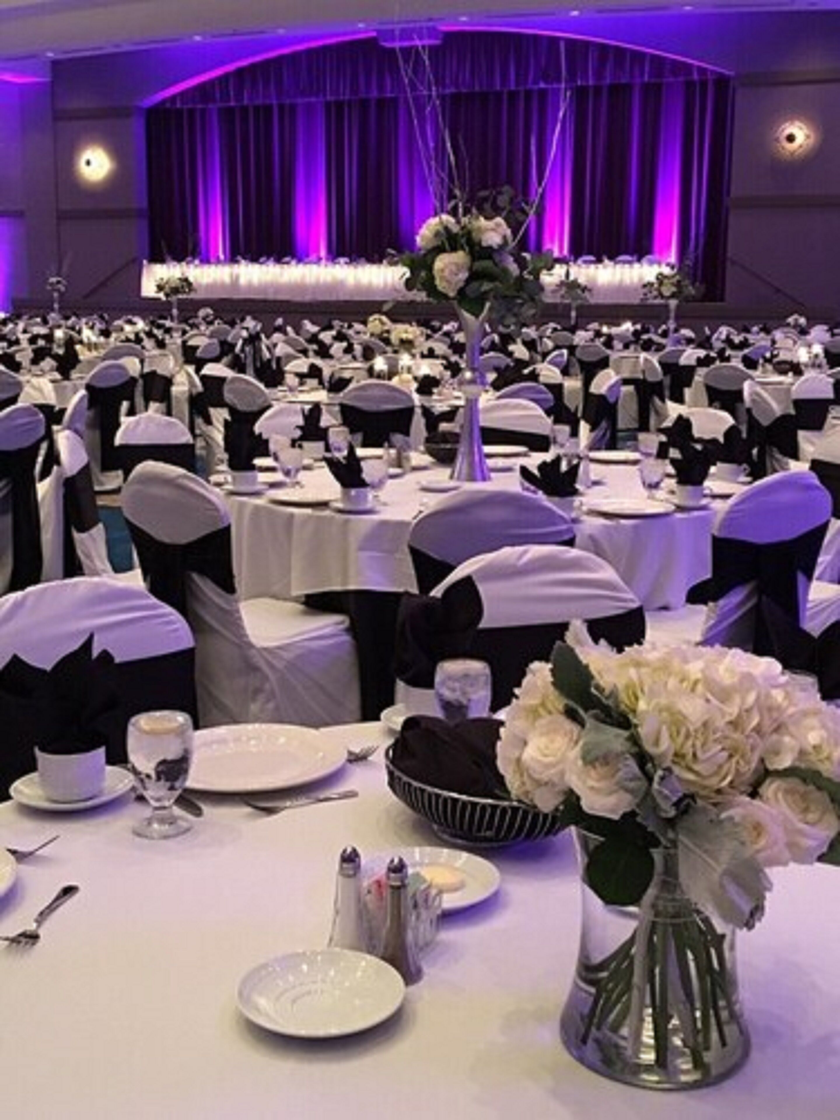 A banquet hall with round tables, black and white tablecloths, and white chairs.