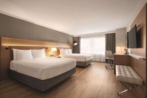 A hotel room with a large bed, a smaller bed, a desk, a chair, a TV, and a window with curtains. - Oneida Casino Hotel (Green Bay)