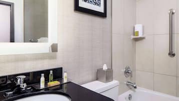 A modern bathroom with a black sink, white toilet, and a bathtub. There is a framed picture on the wall, a towel rack, and a shelf with toiletries.