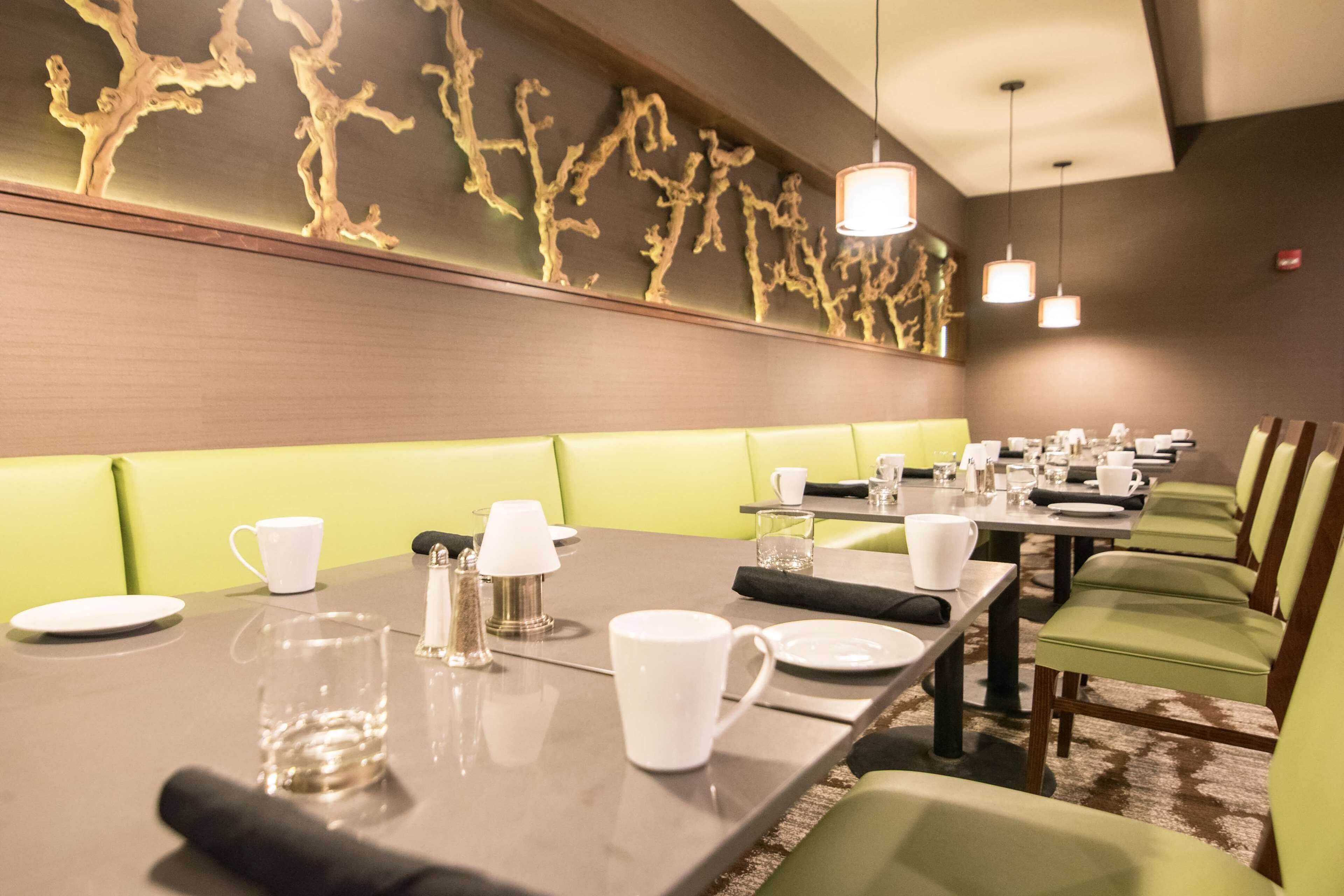 A restaurant with green booths, tables set with white plates, cups, and glasses.