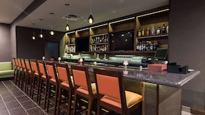 A bar area with a long counter, multiple chairs, and shelves stocked with bottles.