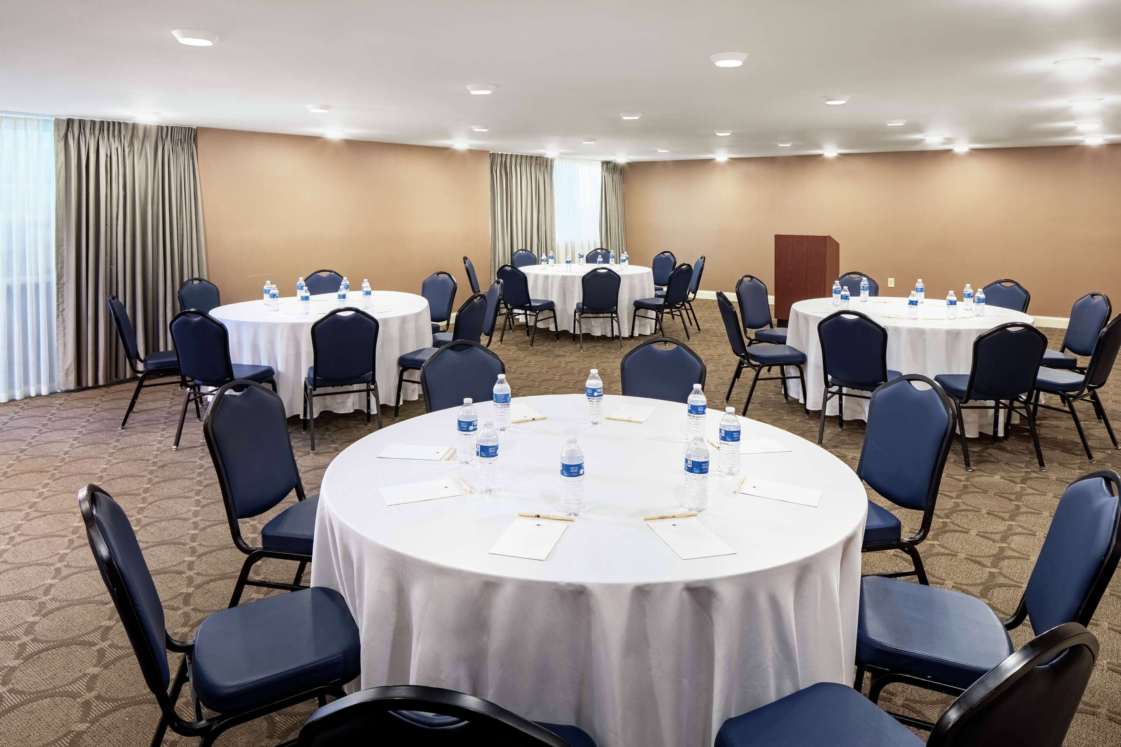 A conference room with multiple round tables, each surrounded by chairs, and water bottles on the tables.