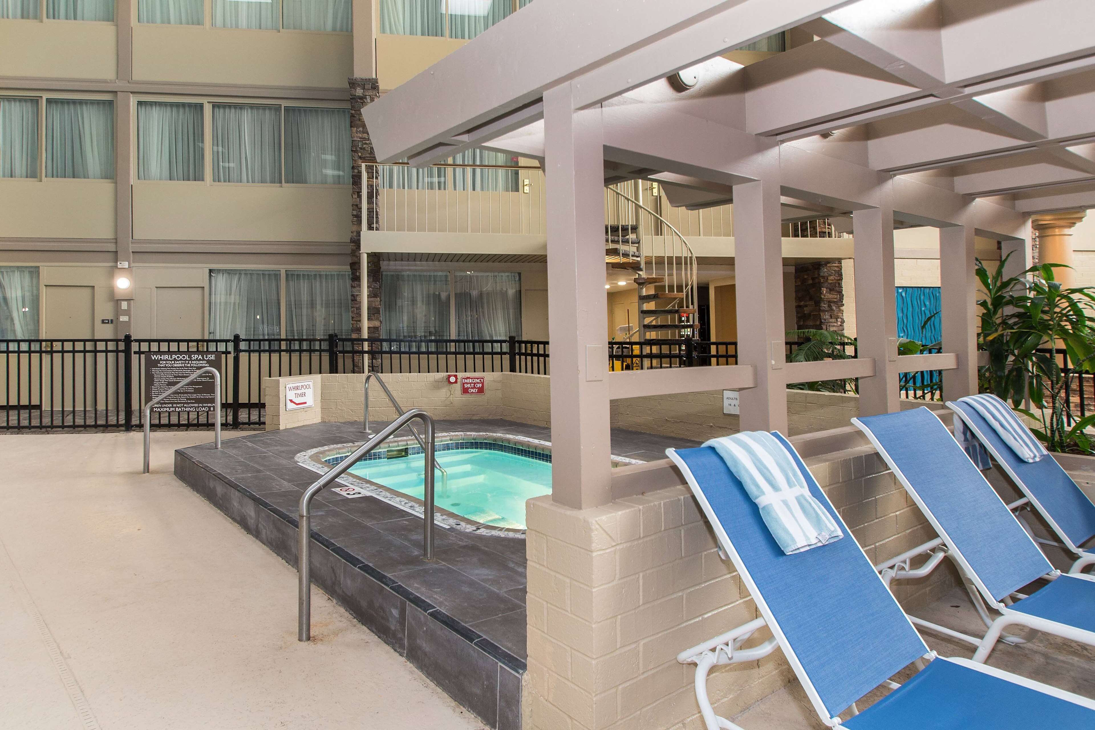 Una piscina interior con sillas de descanso y un jacuzzi, rodeada por un edificio de varios pisos y balcones.