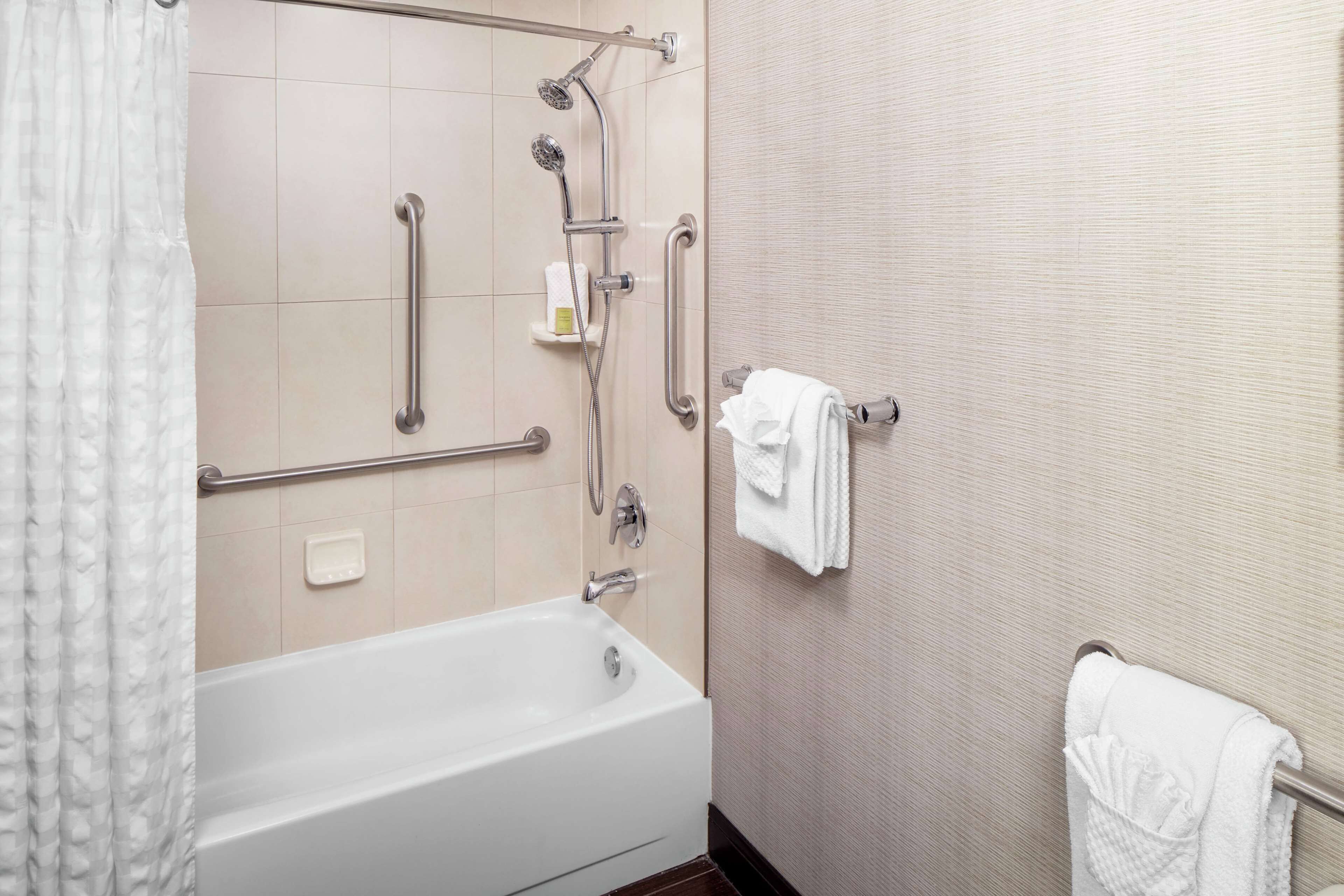 A modern bathroom with a bathtub, shower, and grab bars.