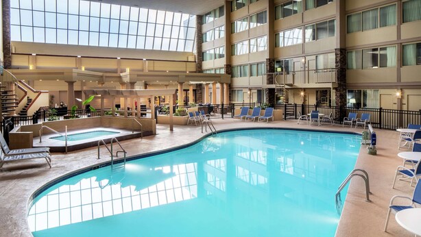 An indoor swimming pool with a sunlit atrium, lounge chairs, and a staircase.