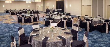 A banquet hall with round tables set for dining, featuring black and white tablecloths and chairs with black and white sashes.