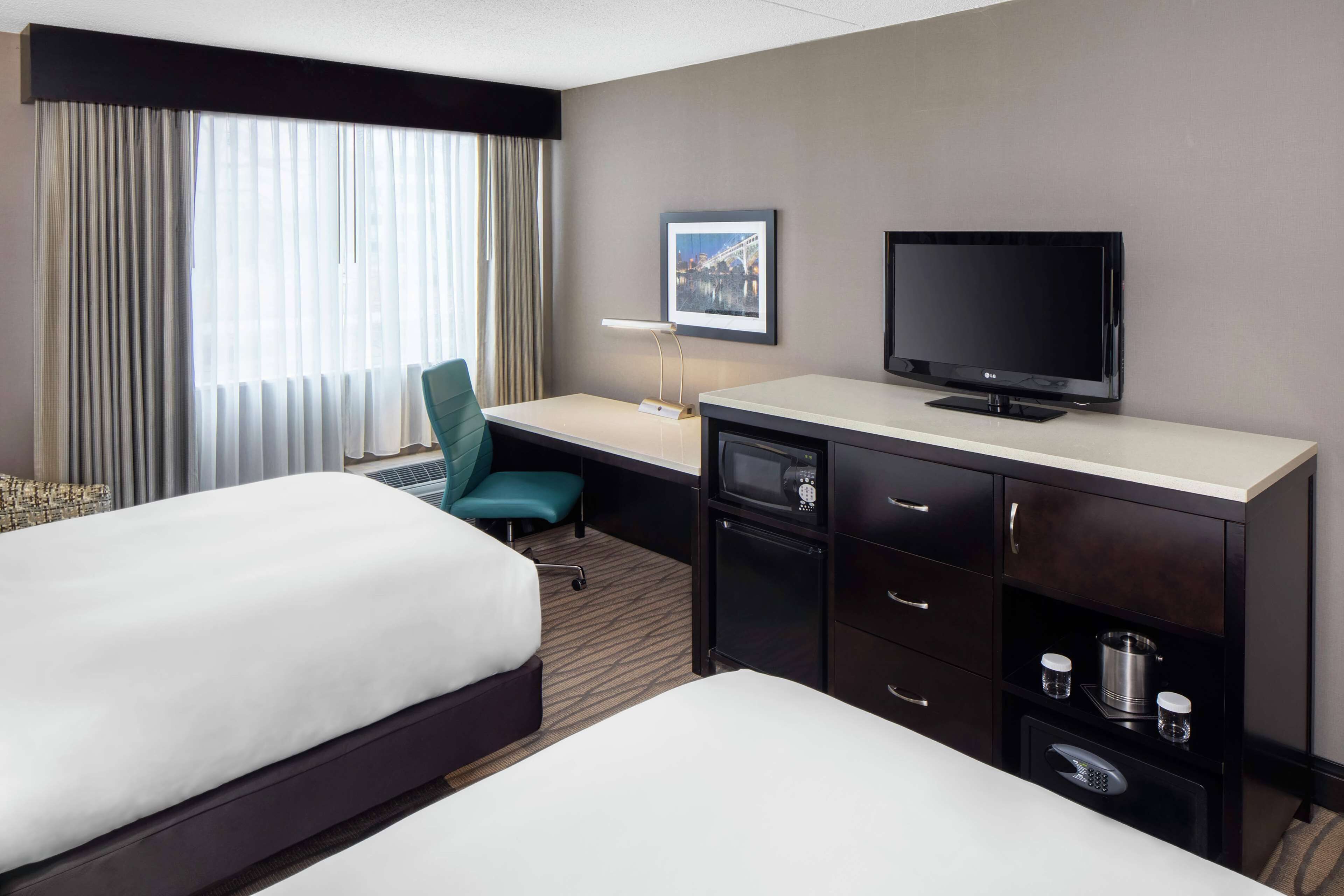 A hotel room with two beds, a desk with a TV, a chair, and a minibar.