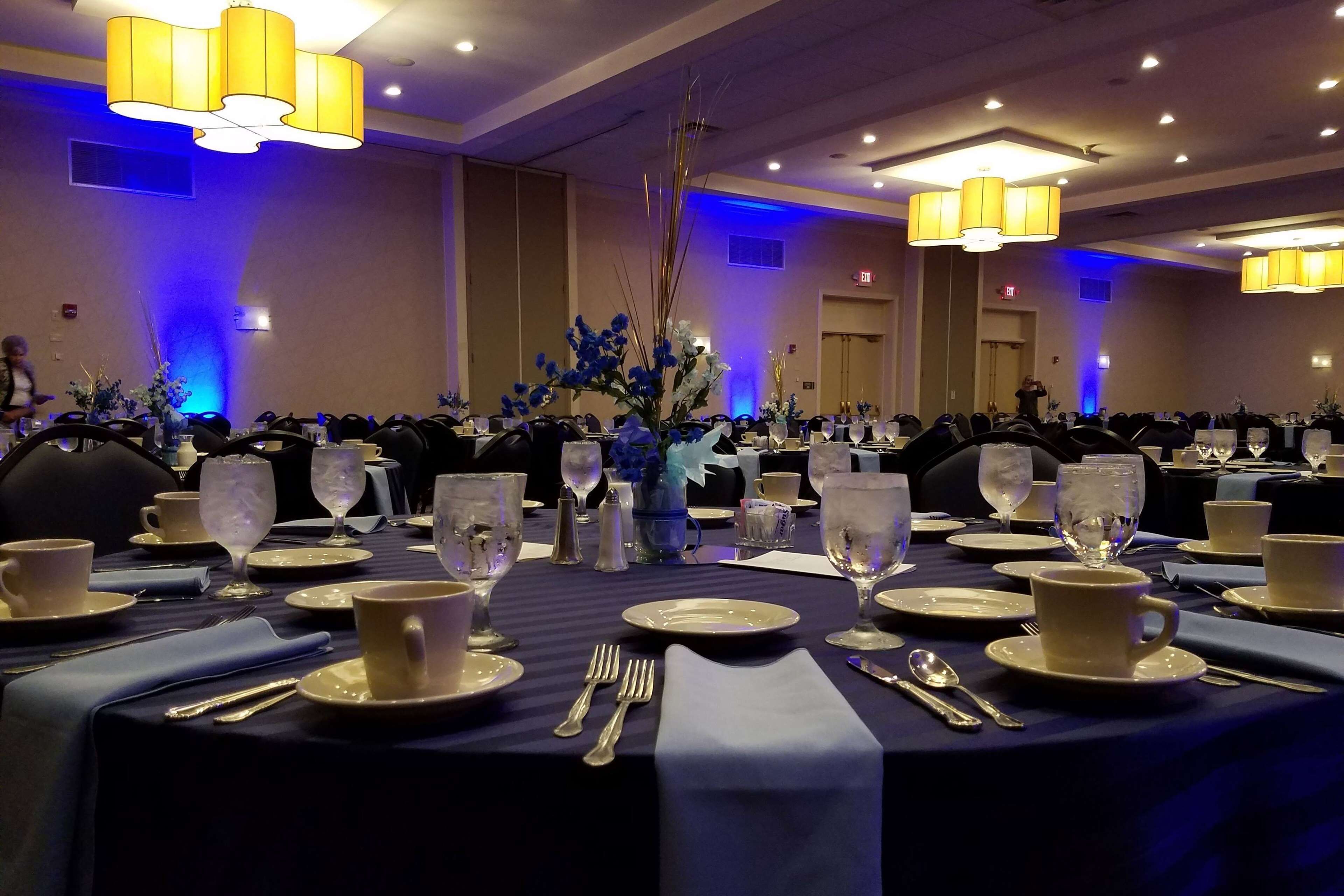 A banquet hall with tables set for a formal event, featuring blue tablecloths, white plates, and clear glassware.