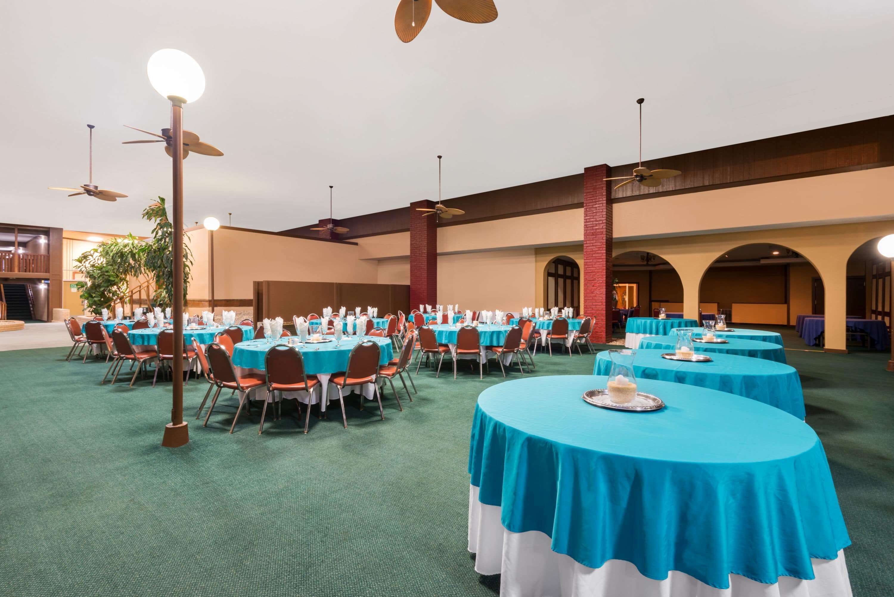 Une salle de banquet avec des tables rondes recouvertes de nappes bleues, disposées en rangées.