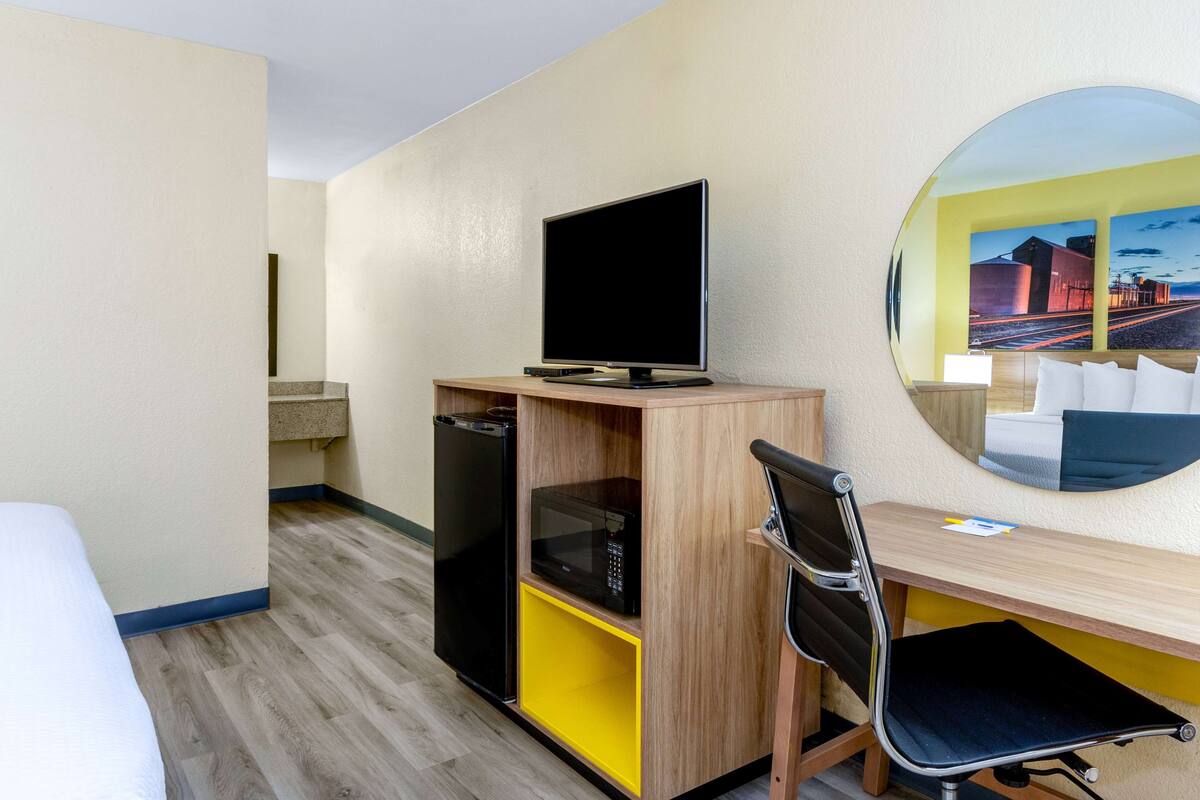 Quarto de hotel com cama, escrivaninha, computador, micro-ondas e frigorífico.