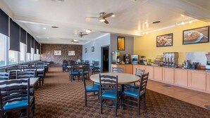A hotel dining area with multiple tables and chairs, a kitchen counter, and a stone wall. - Days Inn & Suites by Wyndham Clovis (Clovis)