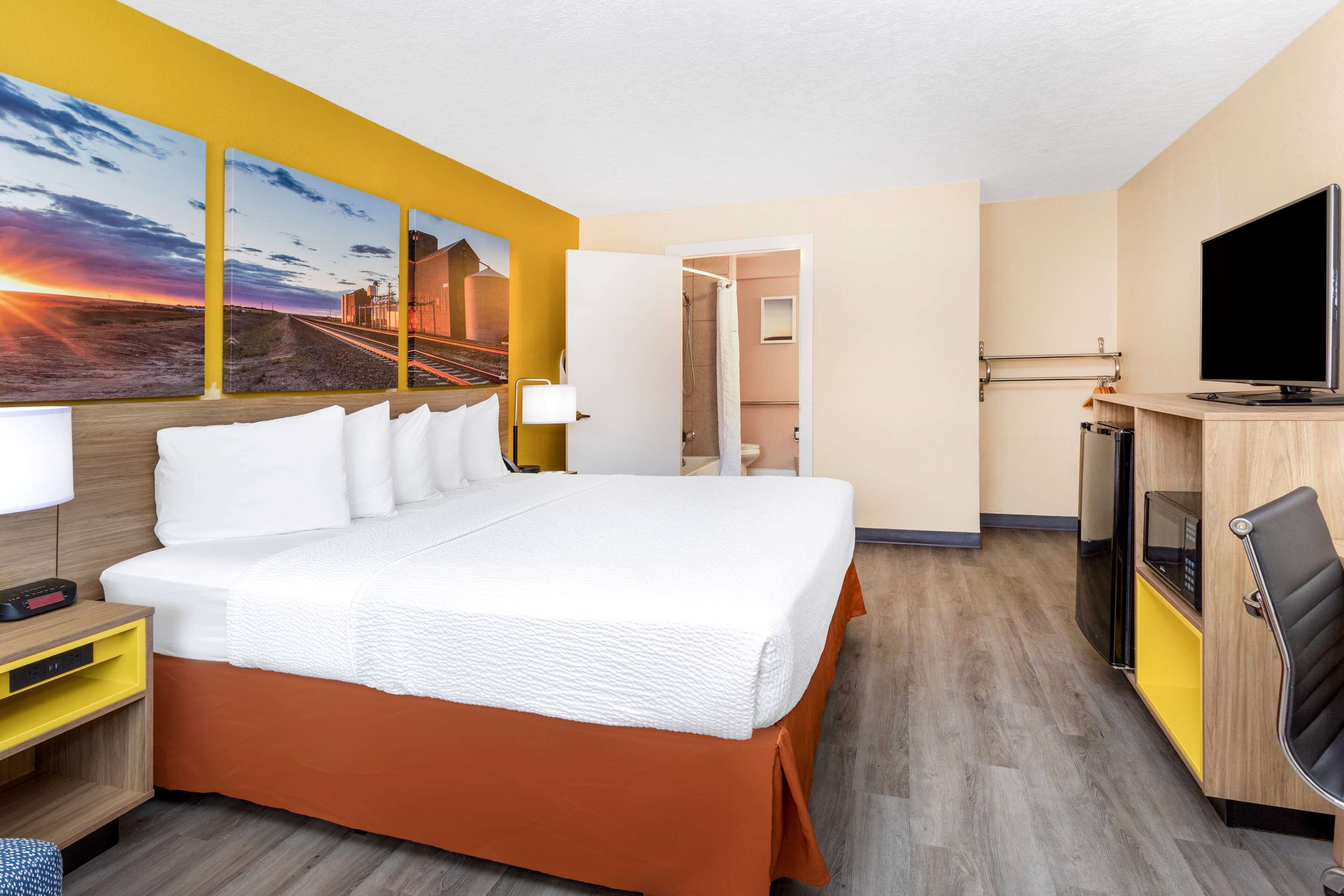 A hotel room with a large bed, a TV, a desk, and a bathroom visible through an open door.