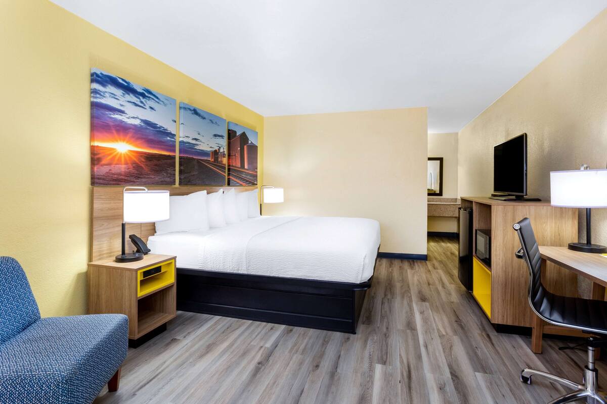 Quarto de hotel com cama, mesas de cabeceira, escrivaninha, cadeira, televisão e obras de arte na parede.