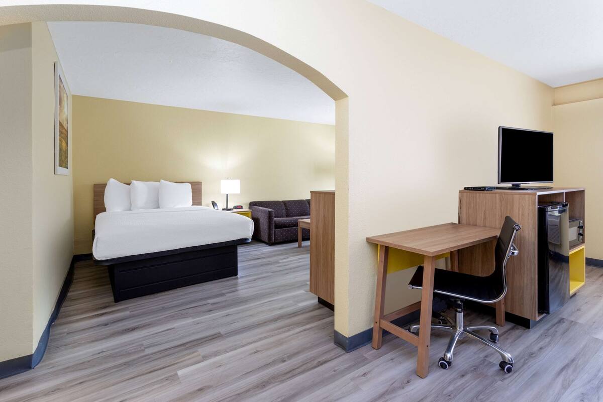 Quarto de hotel com cama, escrivaninha, cadeira, televisão e uma pequena área de estar.