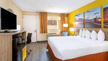 A hotel room with a bed, a desk with a TV, a chair, a window with curtains, an air conditioning unit, and artwork on the wall.