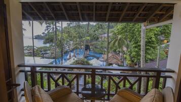 Varanda com móveis de vime e vista para um resort tropical com piscina e palmeiras.