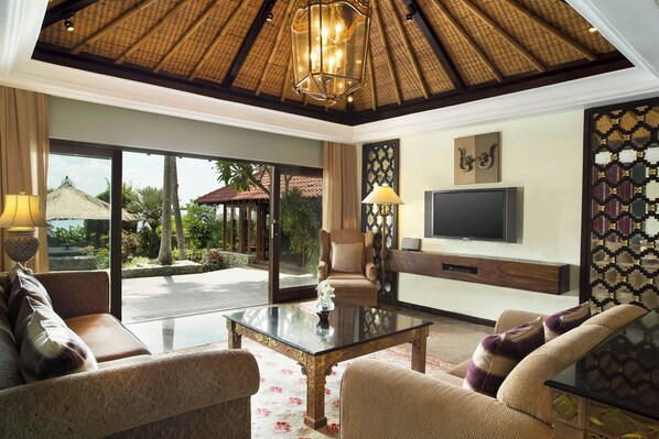A spacious living area with a large glass door leading to an outdoor patio, a comfortable sofa set, a coffee table, and a flat-screen TV mounted on the wall.