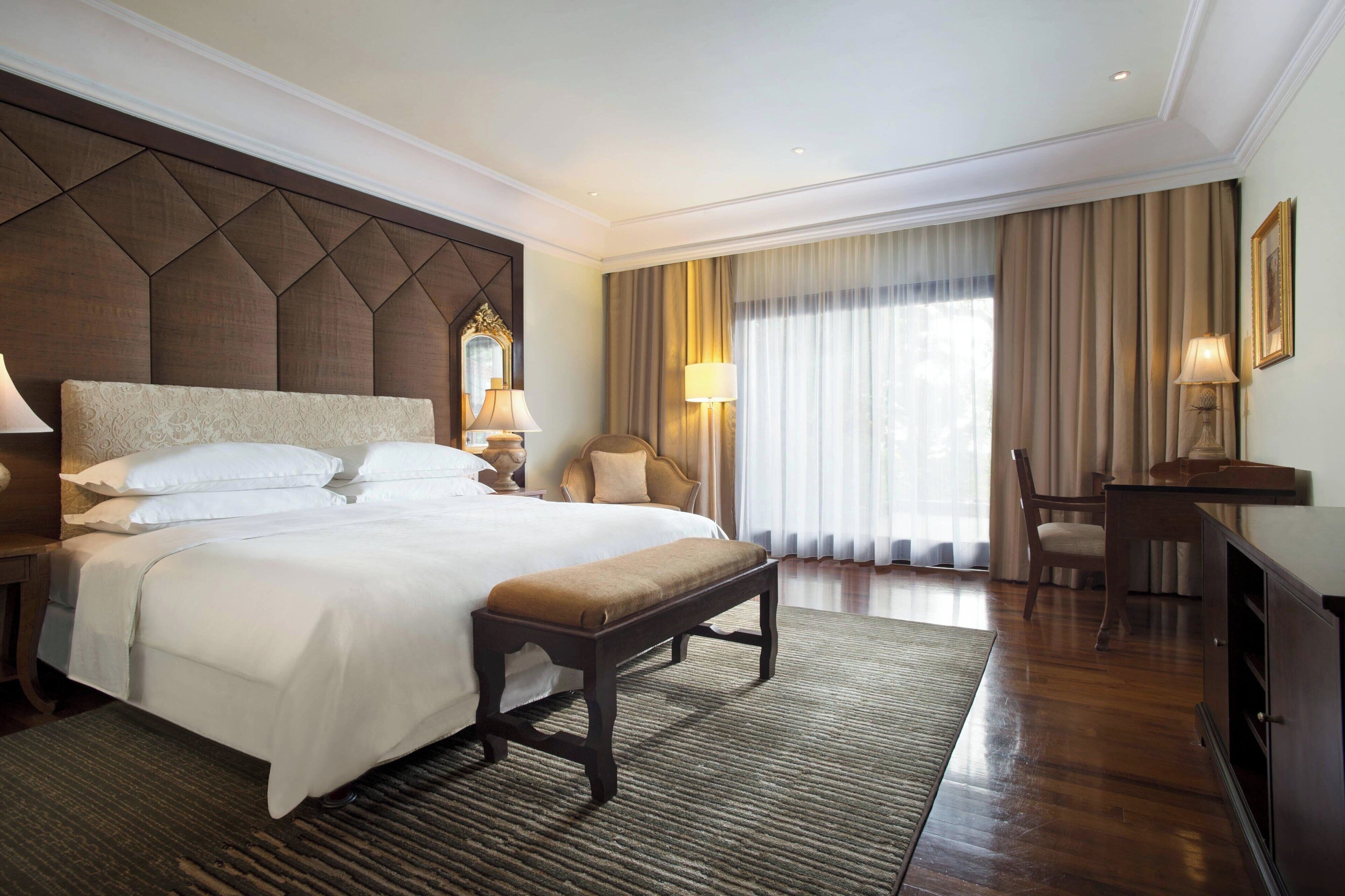 A hotel room with a large bed, a bench, a desk, and a chair.