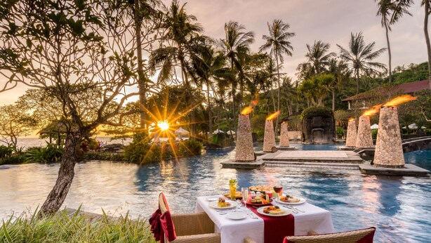 Une table dressée pour deux personnes, avec vue sur une piscine et un coucher de soleil.