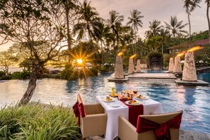 A dining table set for two with a view of a pool and sunset.