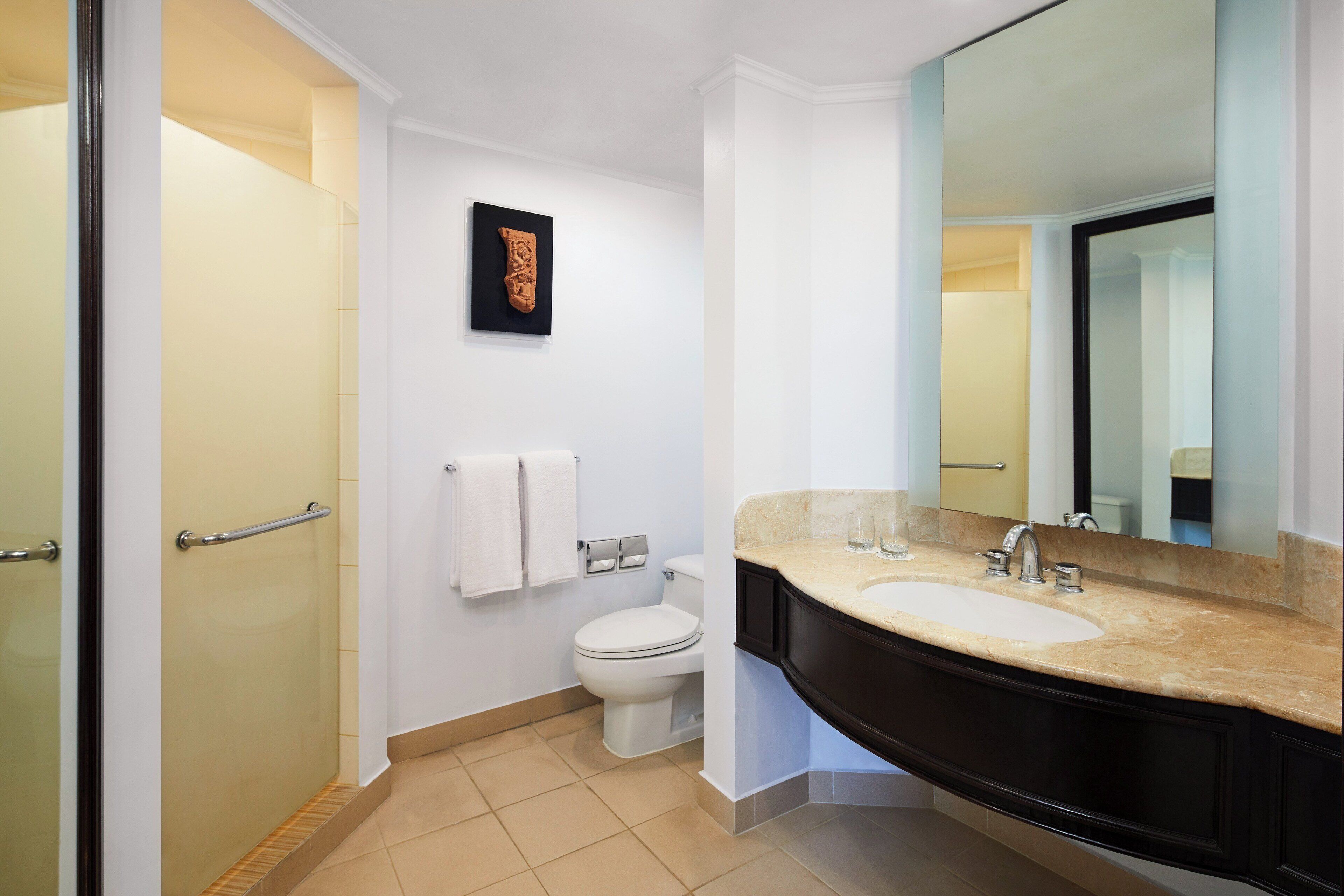 A modern bathroom with a glass shower enclosure, a white toilet, a black vanity with a beige countertop, and a large mirror.