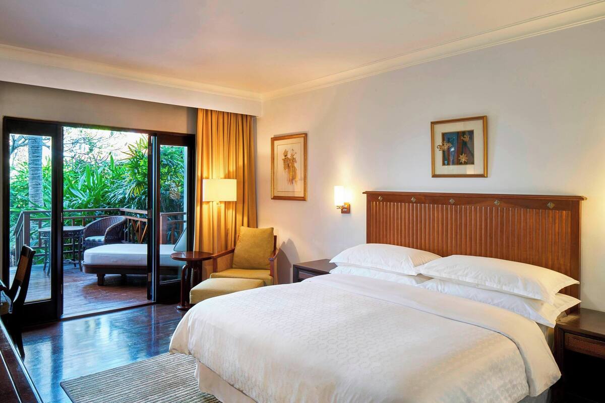 A hotel room with a large bed, a chair, a desk, and a view of the outdoors.