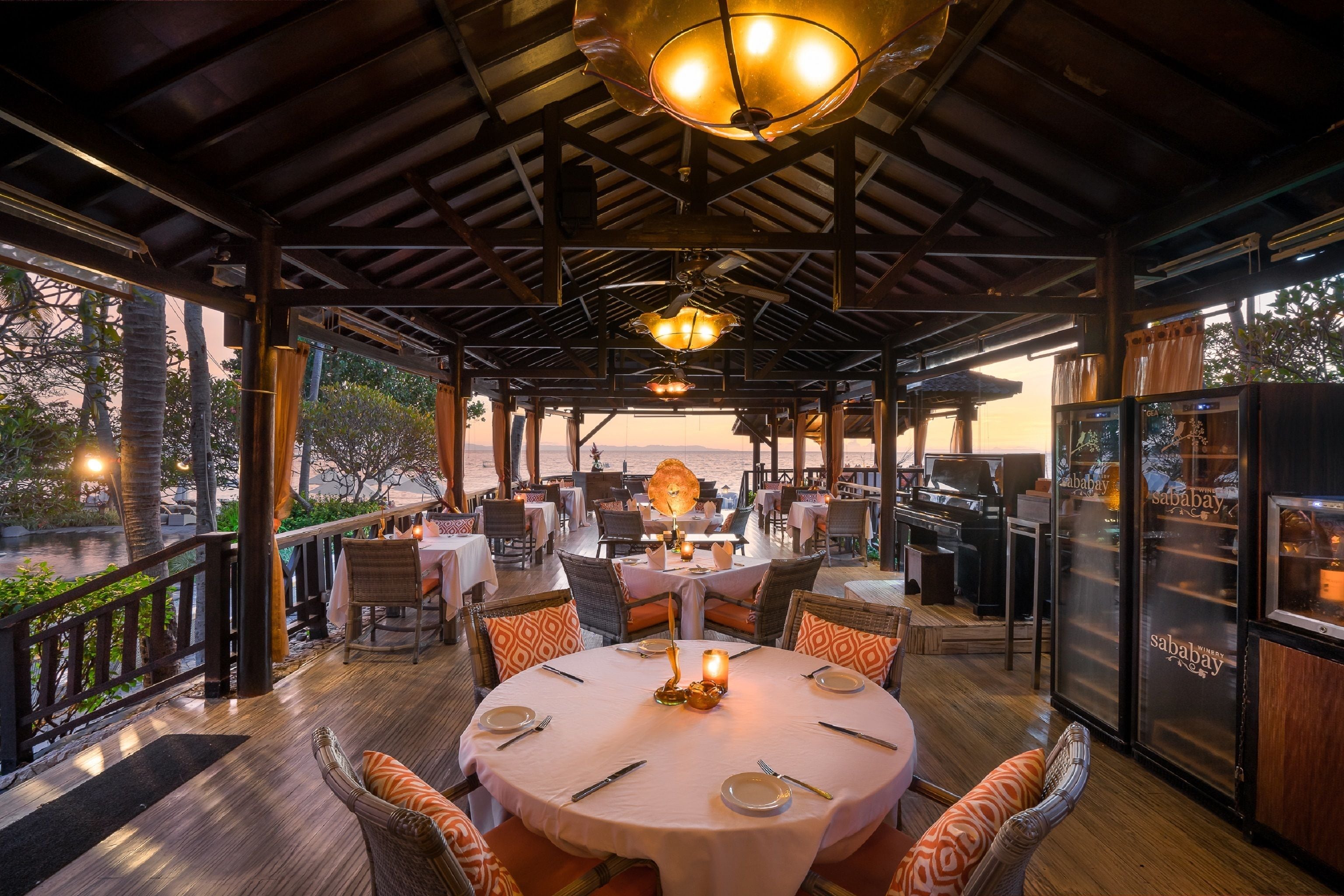 A restaurant with round tables, wicker chairs, and a view of the beach.