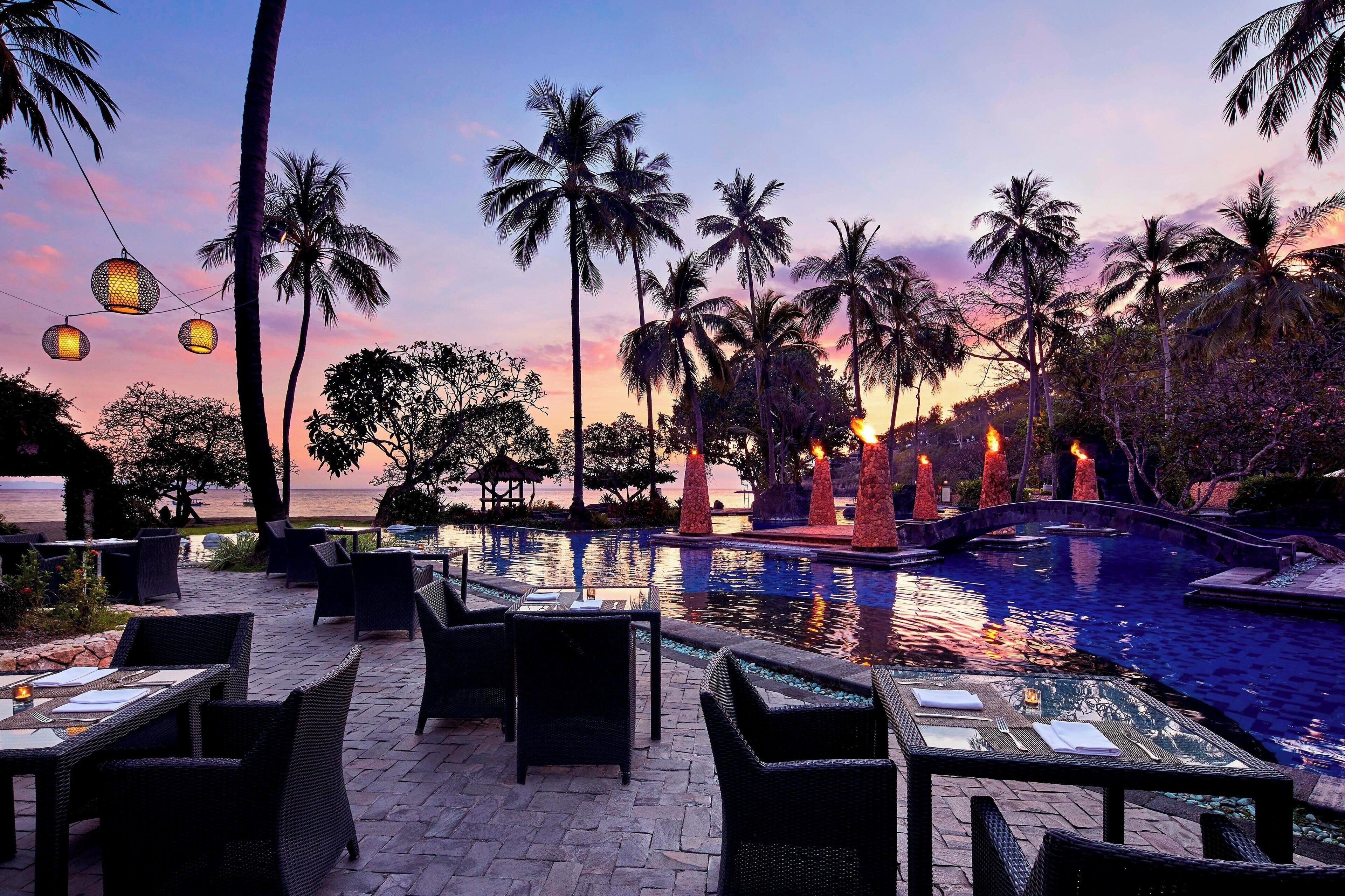 A poolside area with outdoor seating and a view of the ocean at sunset.