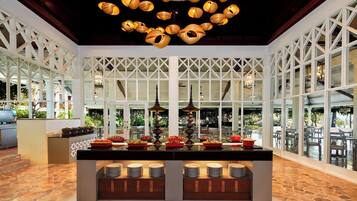 A buffet area with a central island, overhead wooden chandeliers, and large windows offering views of the outdoors.