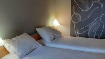 A hotel room with a bed, pillows, a nightstand, a lamp, and a wall with a chalkboard drawing.