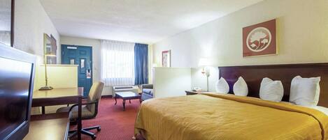 Ein Hotelzimmer mit Bett, Schreibtisch, Stuhl, Fernseher und einem Fenster mit Vorhängen.