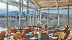 En restaurant med dækkede borde, store vinduer der viser bjergudsigt, og orange stole.