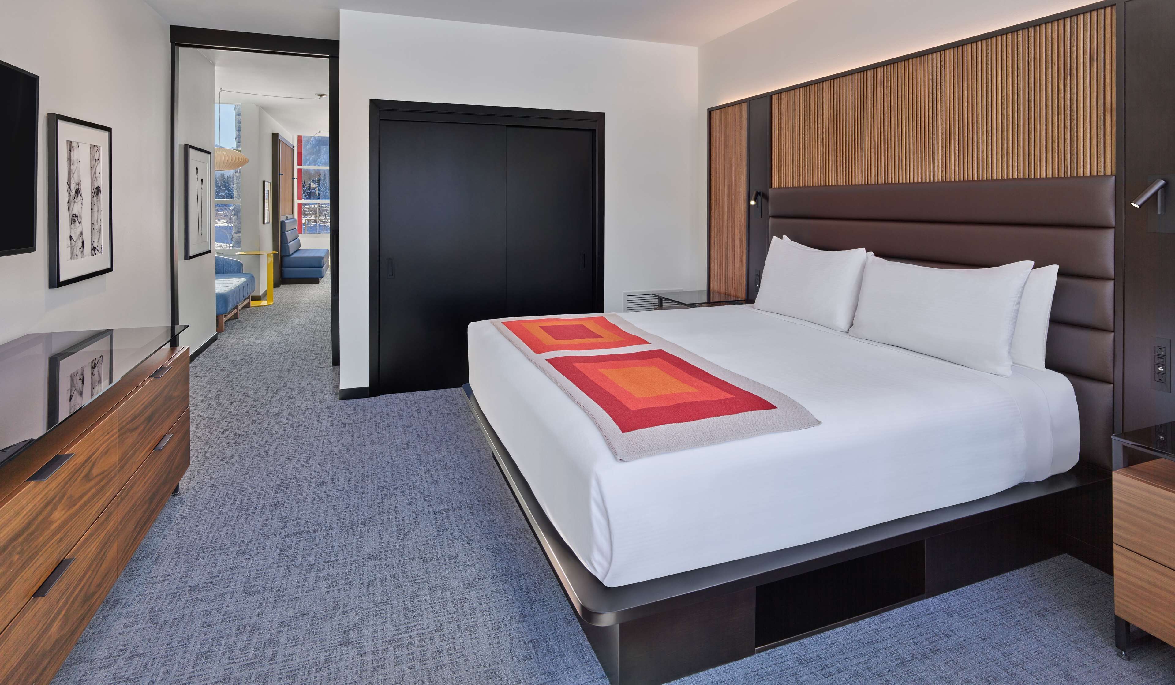 Une chambre d’hôtel moderne avec un grand lit, une tête de lit en bois, un bureau et une vue sur la ville par la fenêtre.