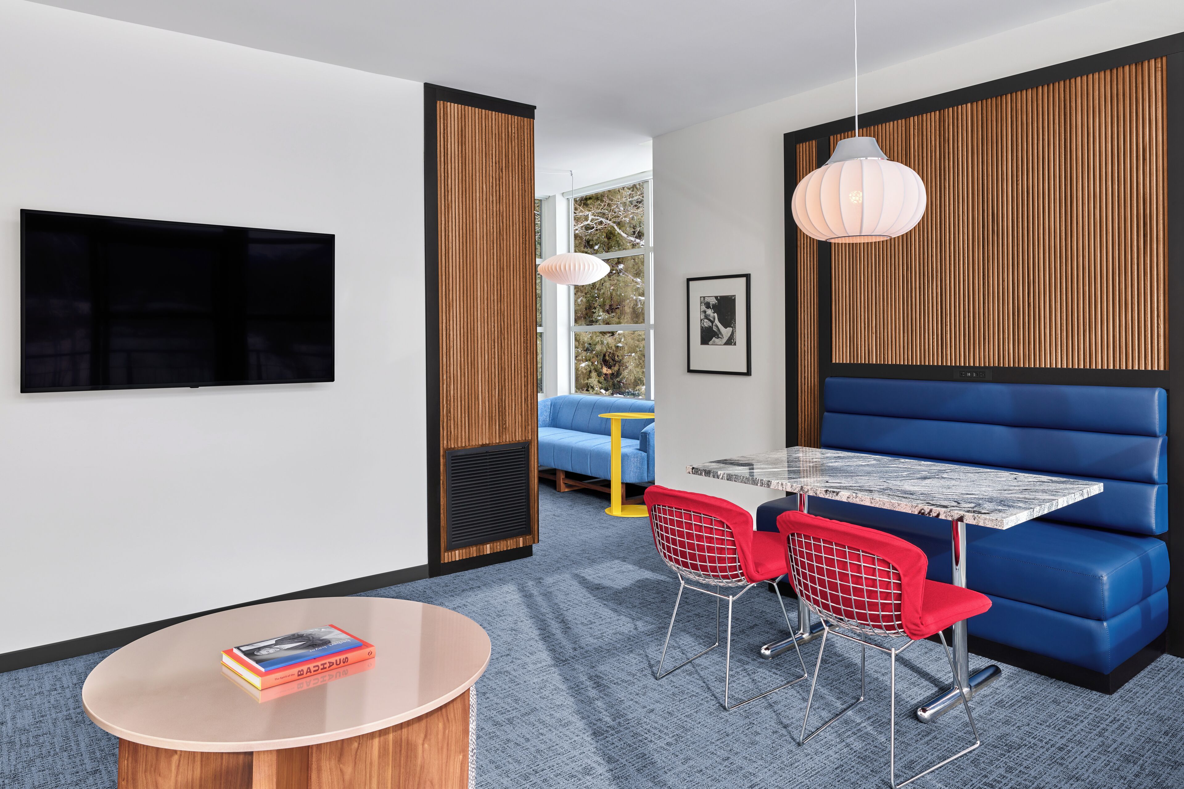 A modern room with a TV, a round table, red chairs, a blue sofa, and a wooden accent wall.