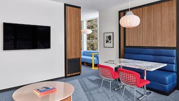 Una habitación moderna con televisión, una mesa redonda, sillas rojas, un sofá azul y una pared de madera decorativa.