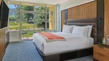 Een moderne hotelkamer met een groot bed, een houten hoofdeinde, een televisie en uitzicht op het omliggende landschap.
