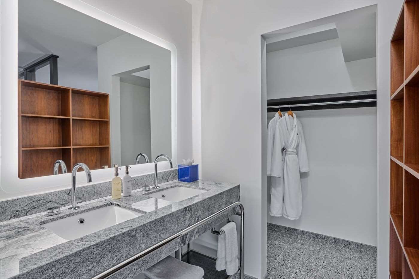 Ein modernes Badezimmer mit einem großen Spiegel, zwei Waschbecken und einem begehbaren Kleiderschrank mit Holzböden.