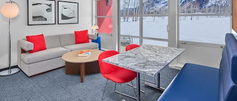 A modern room with a sofa, red chairs, a marble table, and a large window with a snowy mountain view.