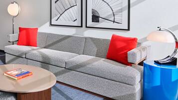 A modern living room with a grey sofa, red cushions, a round coffee table, and two framed abstract artworks on the wall.